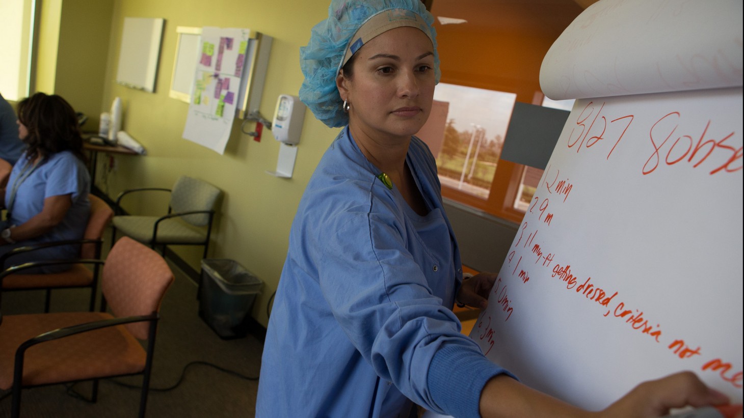 Health care worker in blue hairnet writing on a flip chart 