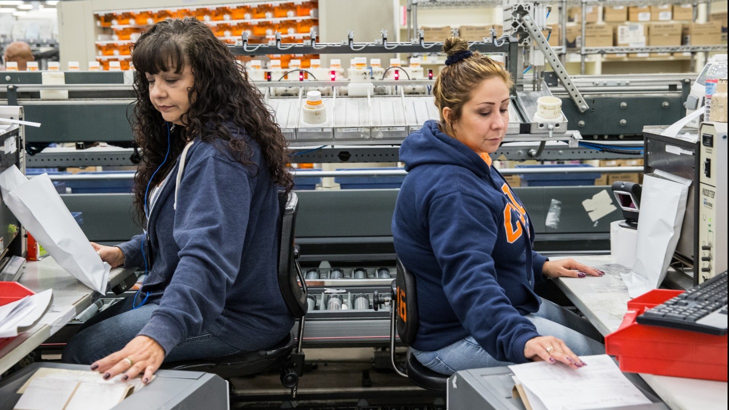 Two women, sitting back to back, entering data into a computer