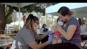 Nurse administers vaccine to child on mother's lap